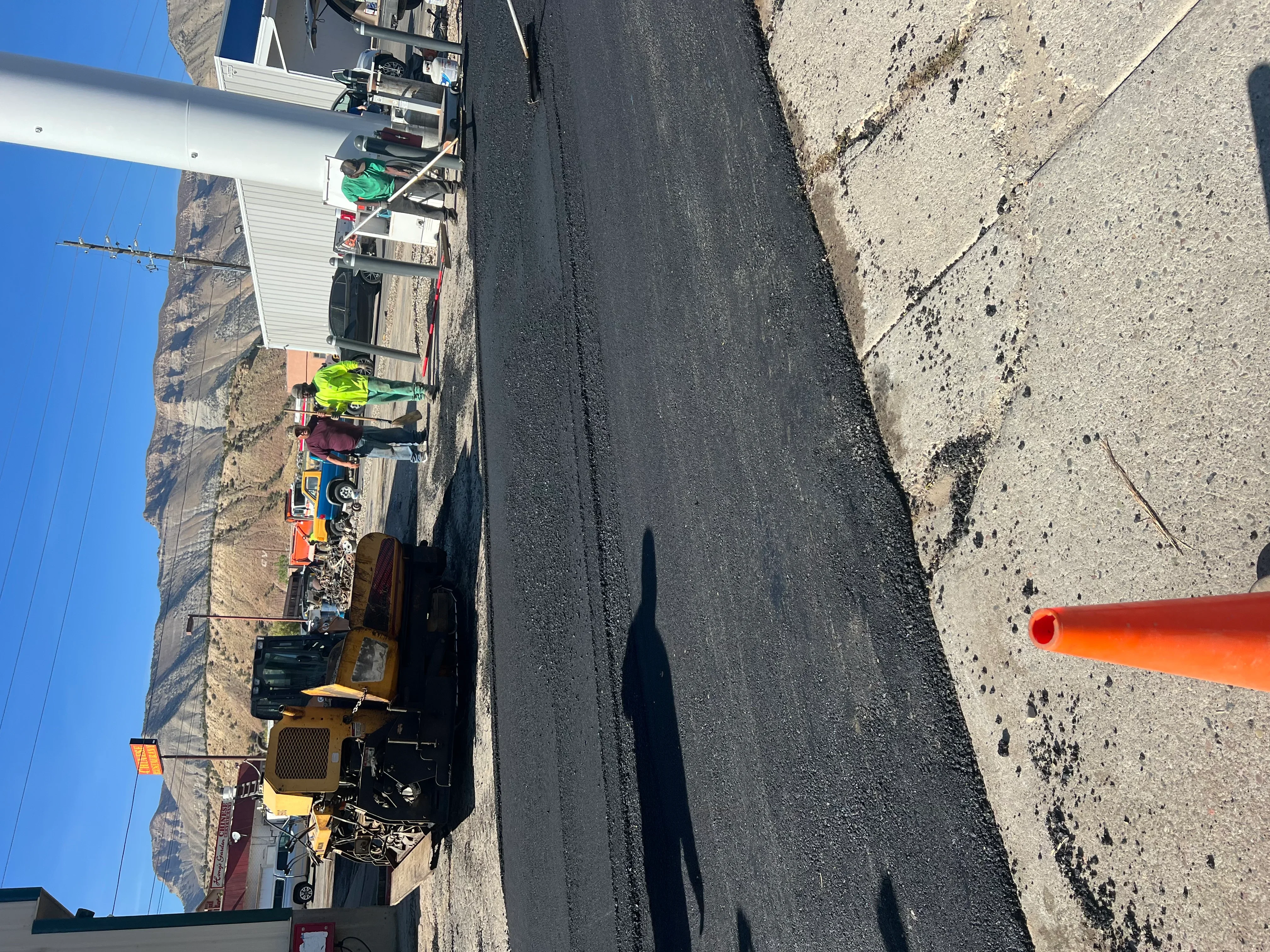 Asphalt paving machine laying fresh black asphalt with crew members in safety vests
