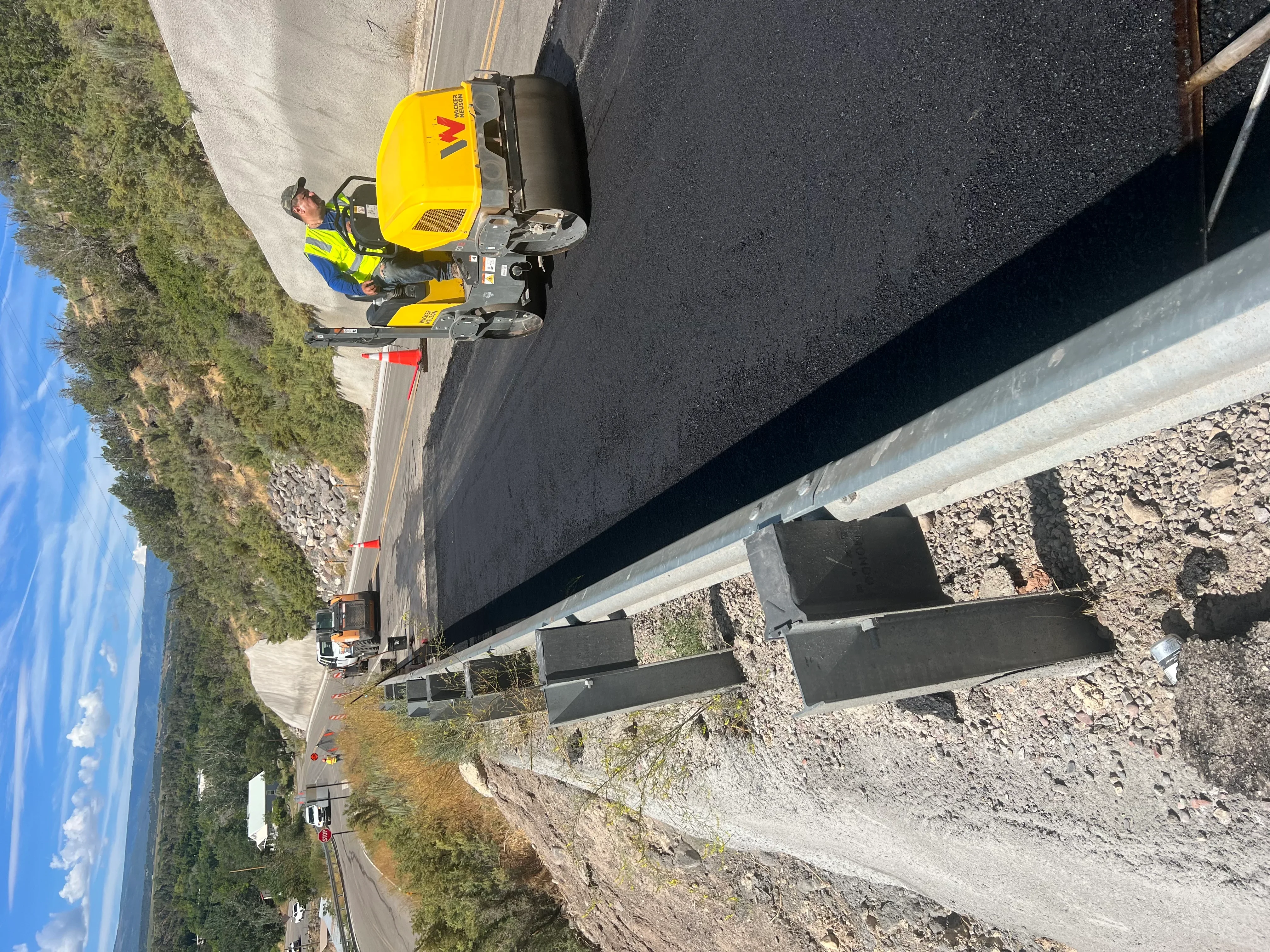 Asphalt paving crew with yellow compactor installing fresh asphalt on residential driveway