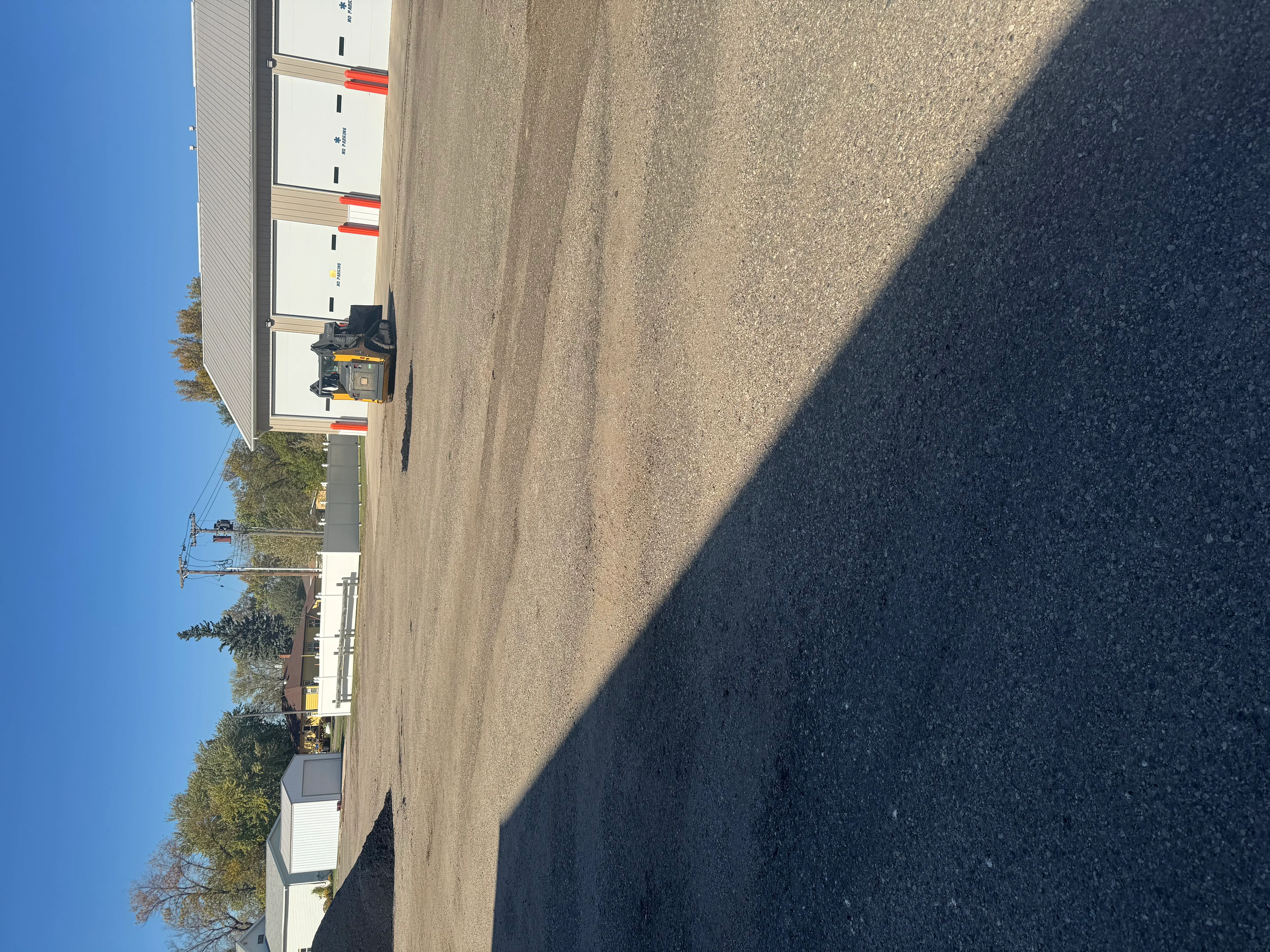 Fresh asphalt paving with dark finish on commercial parking lot next to metal-sided building