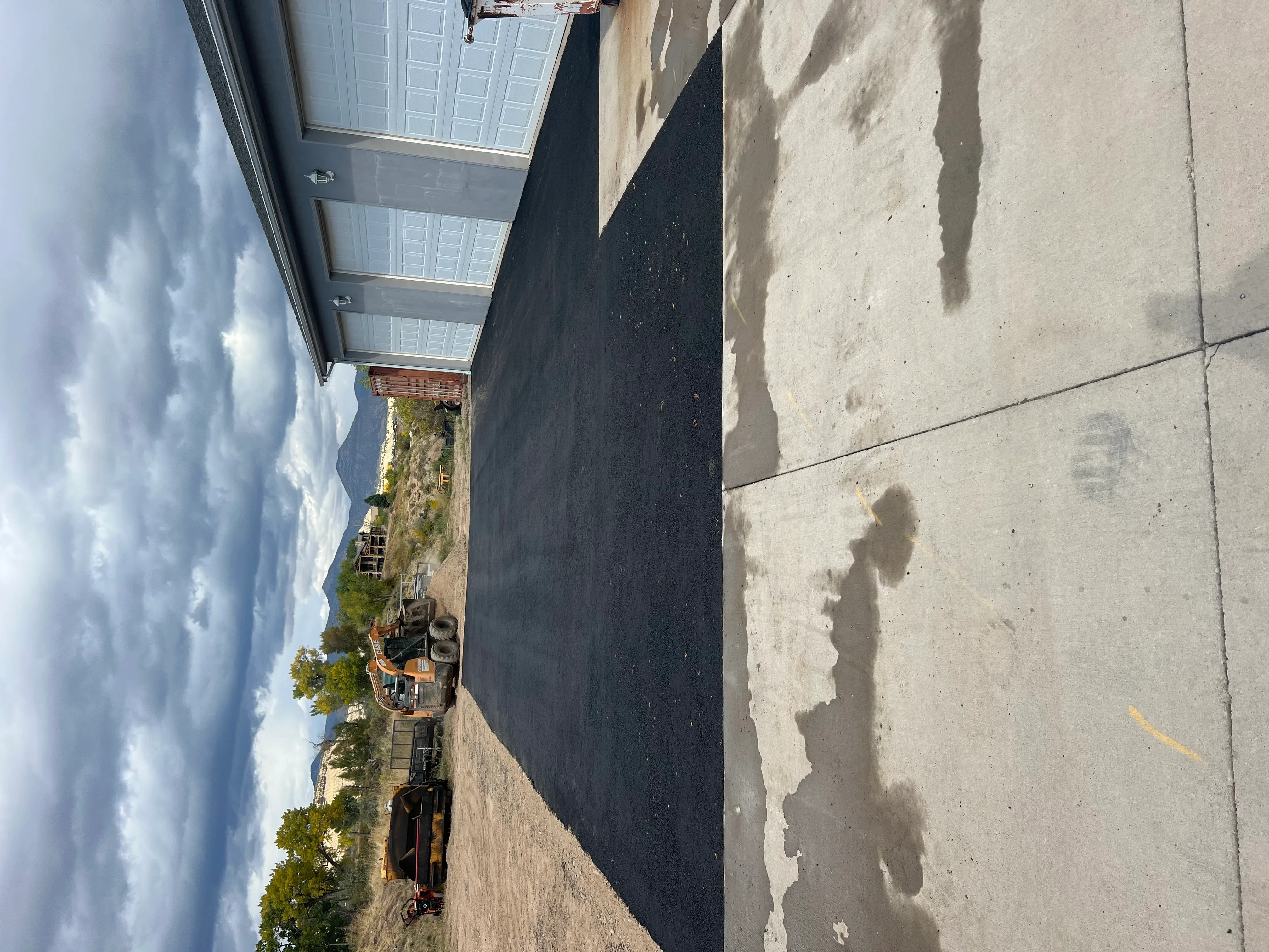 New black asphalt driveway paving with concrete apron and white garage doors
