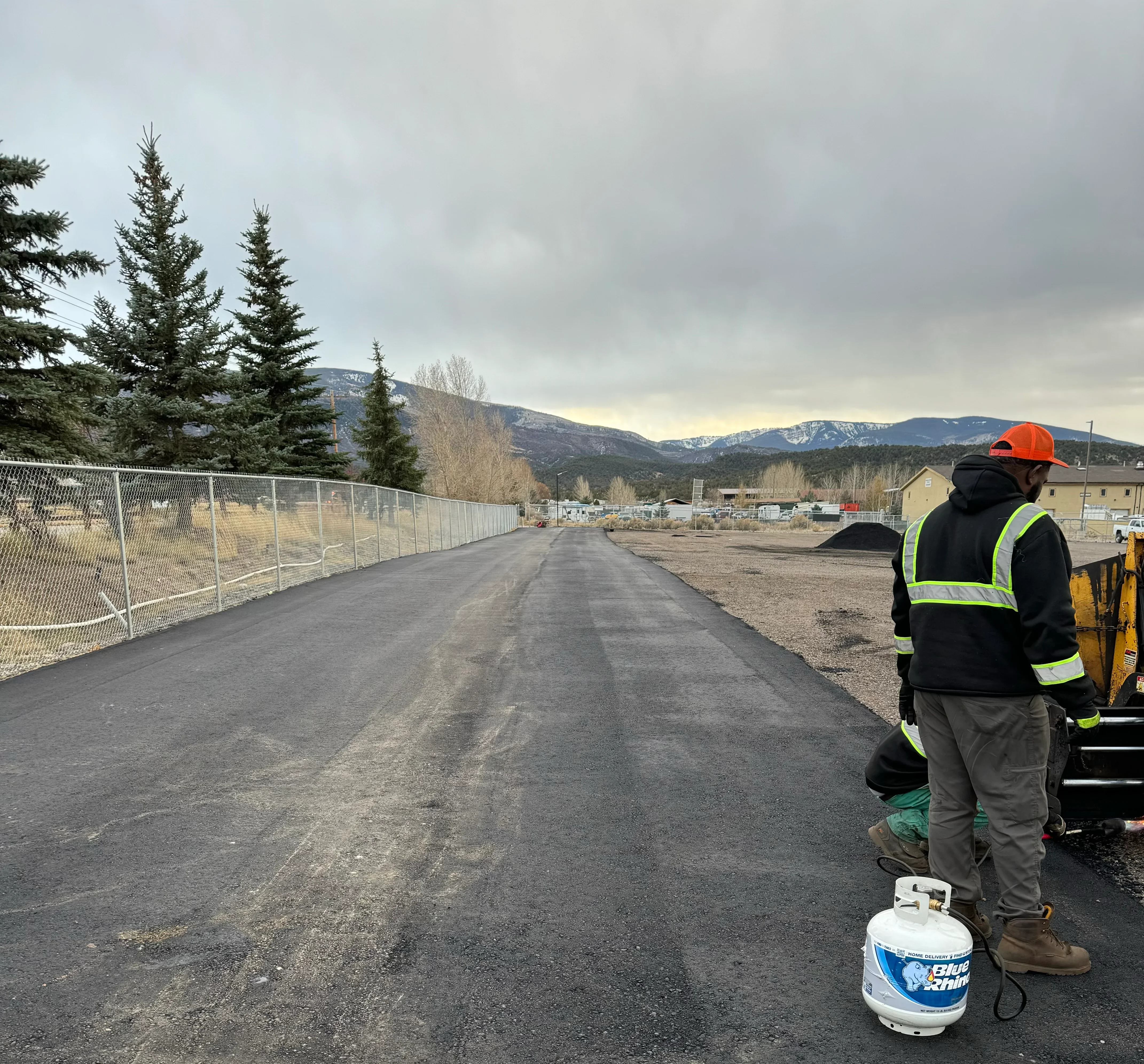 Newly paved asphalt driveway with chain-link fence and construction equipment on-site