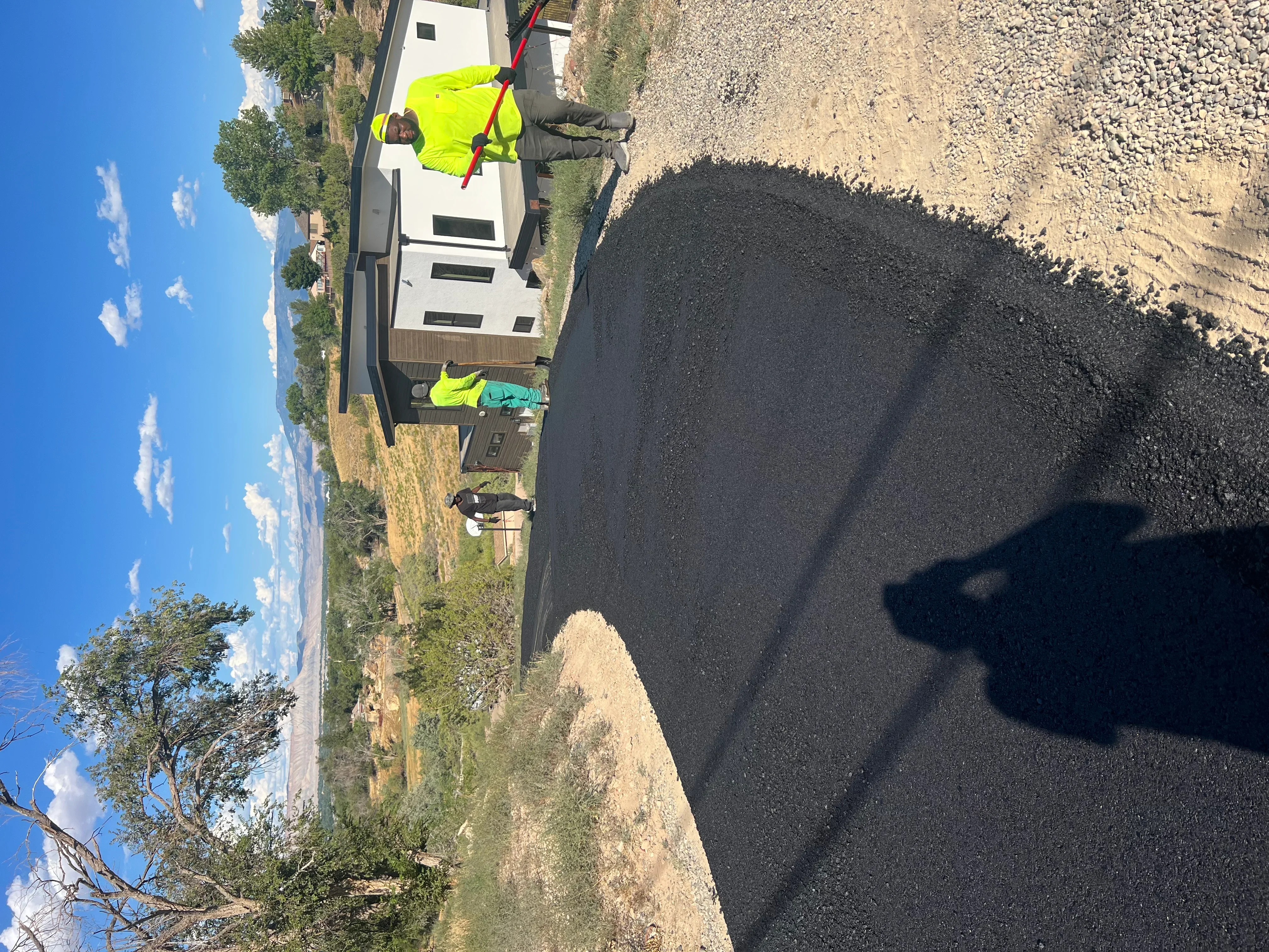 Newly paved black asphalt driveway with crew members in safety vests during installation