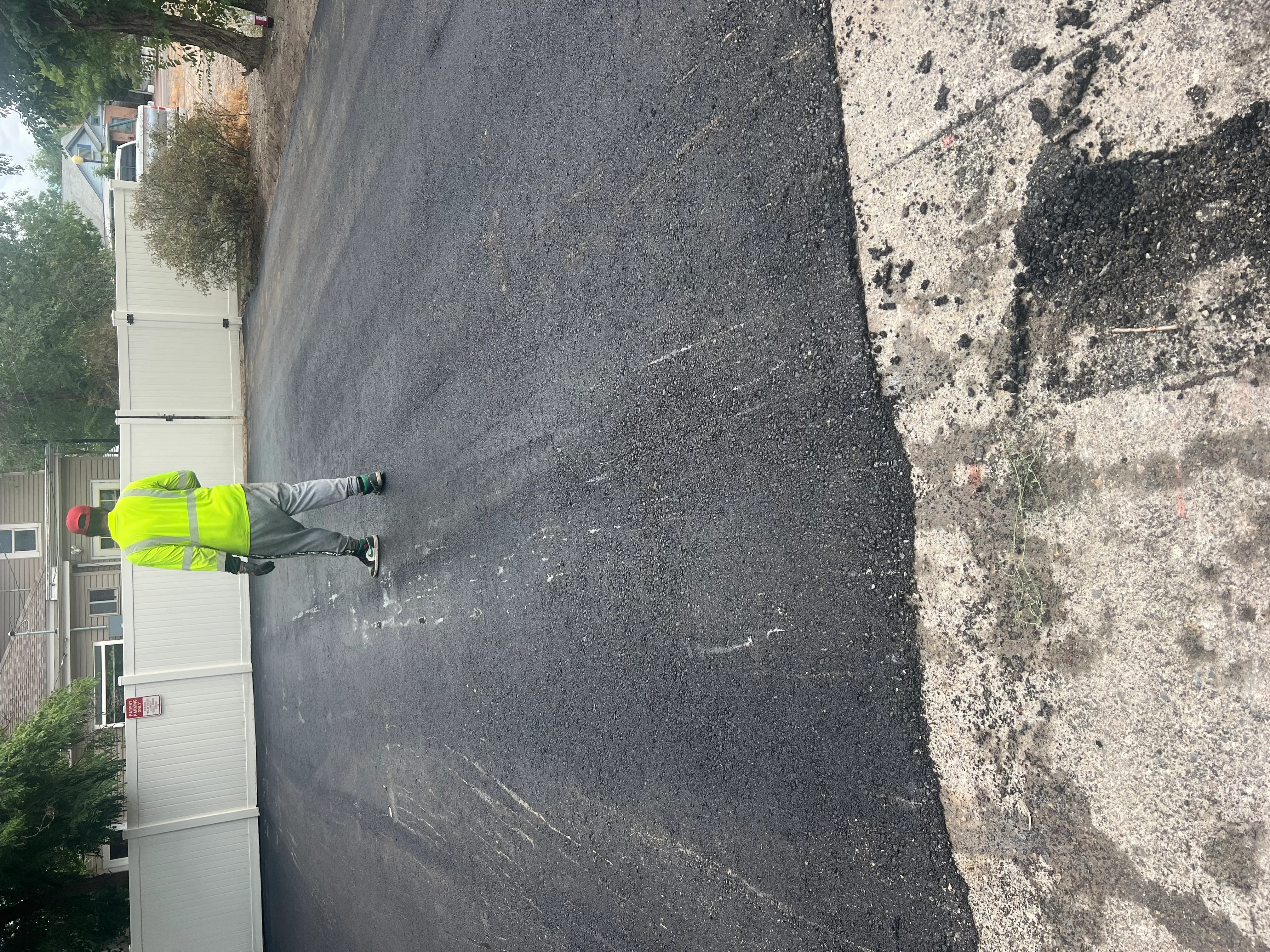 Worker in safety vest inspecting newly paved asphalt driveway next to concrete foundation