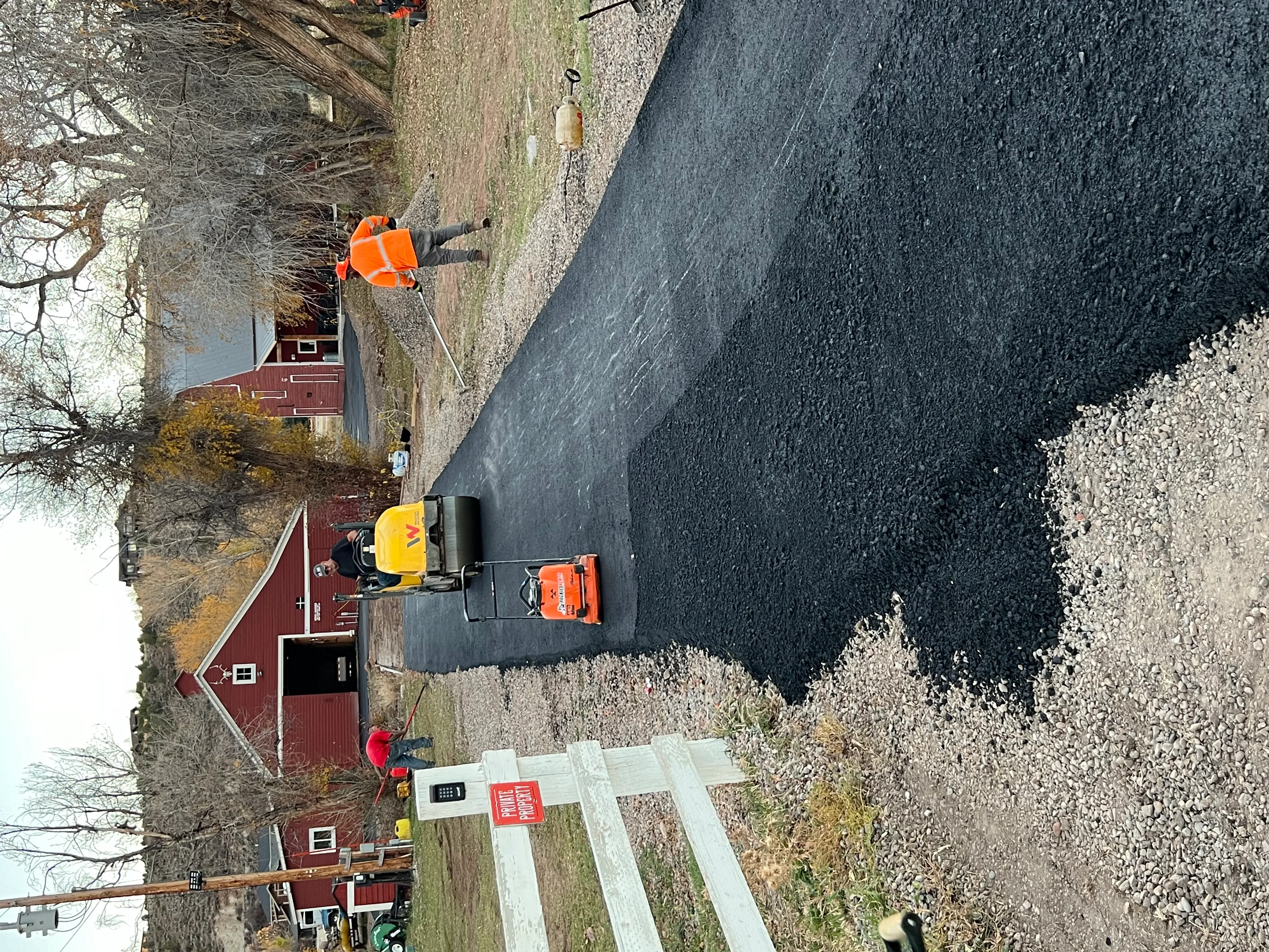 Fresh black asphalt driveway with white gravel borders and stone edging during installation