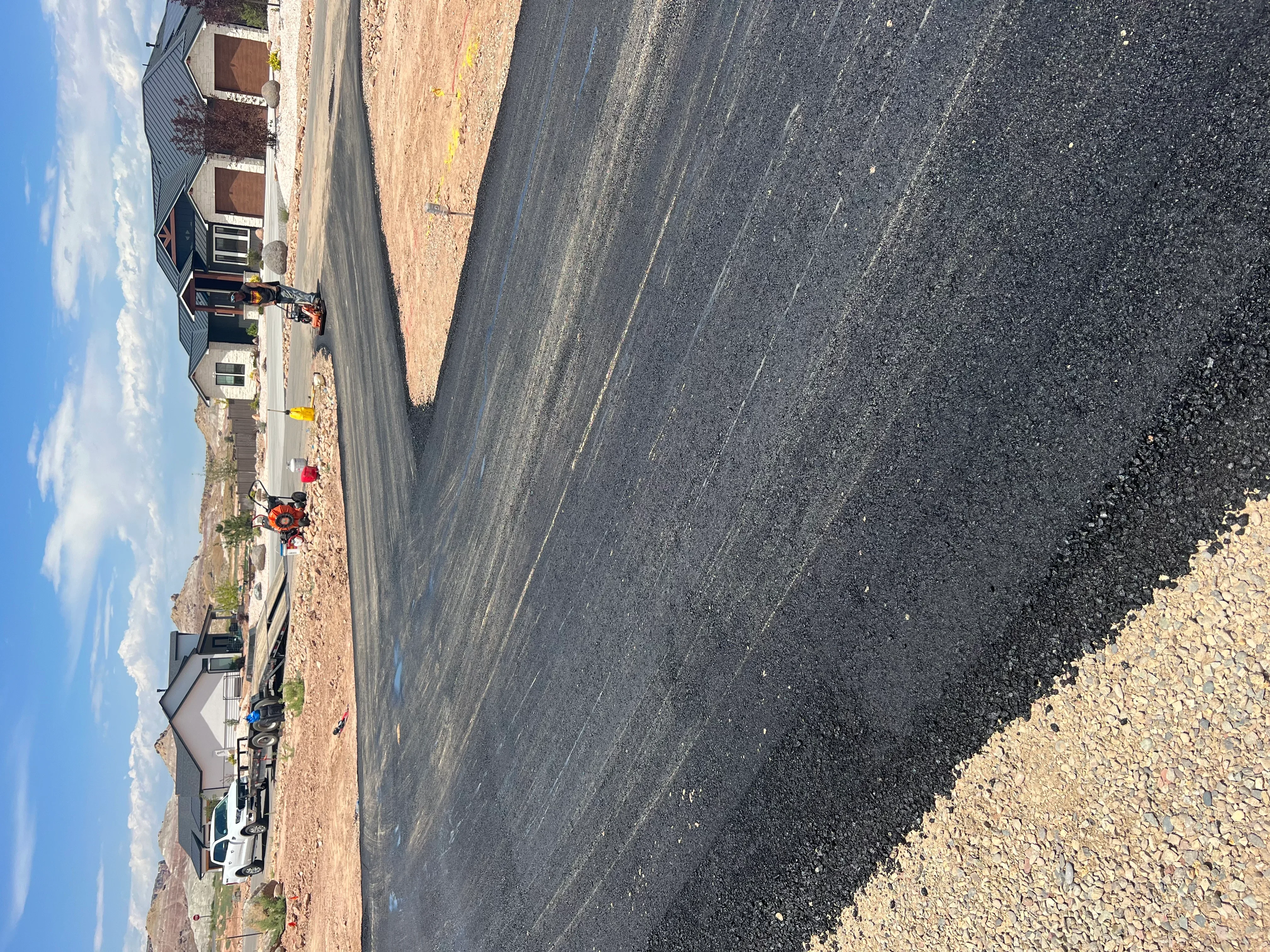 Newly paved asphalt driveway with dark surface and gravel transition edges
