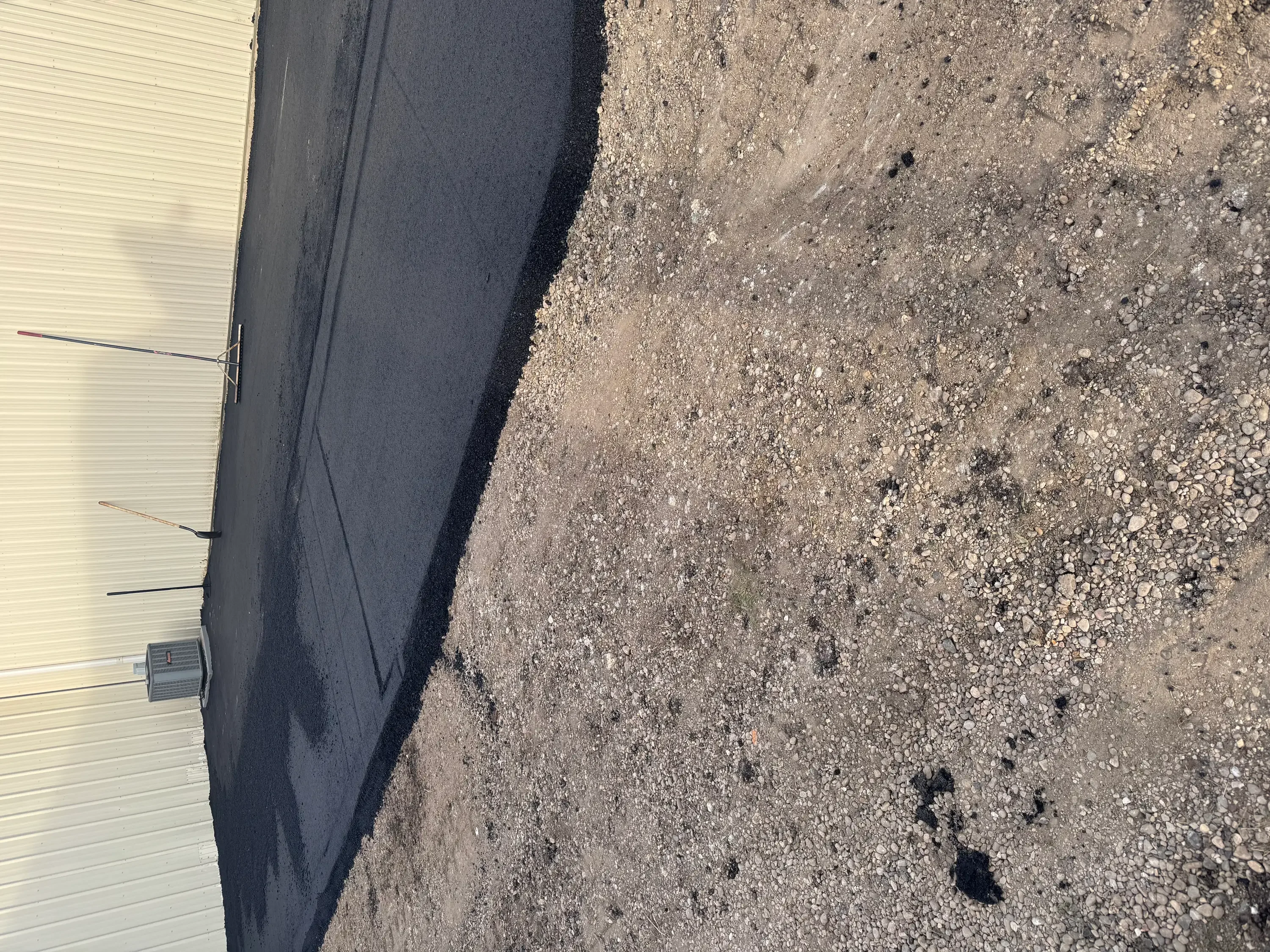 New asphalt paving next to metal building with proper edge detail and compaction