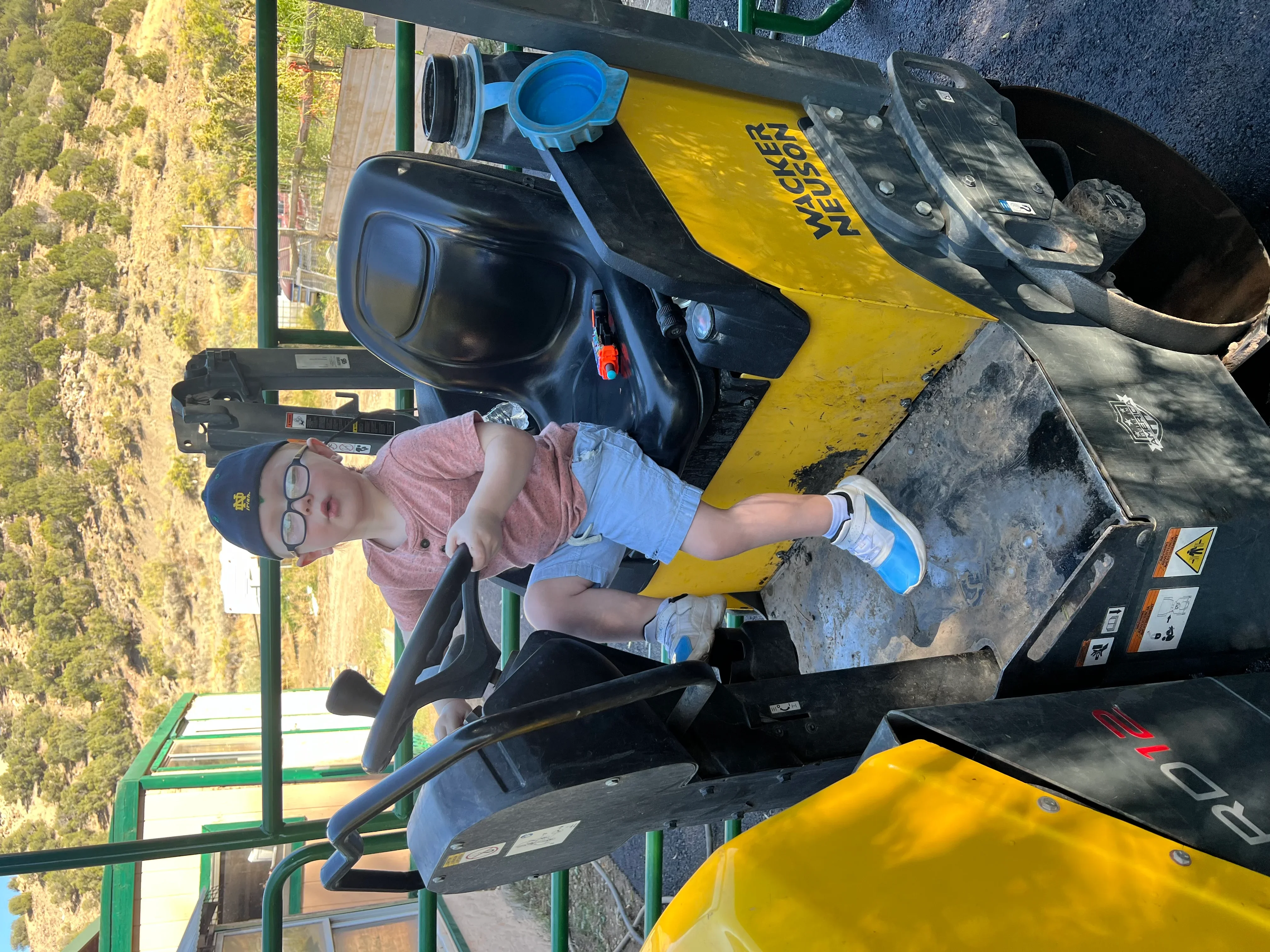 Operator controlling yellow asphalt paver with dual drums on job site