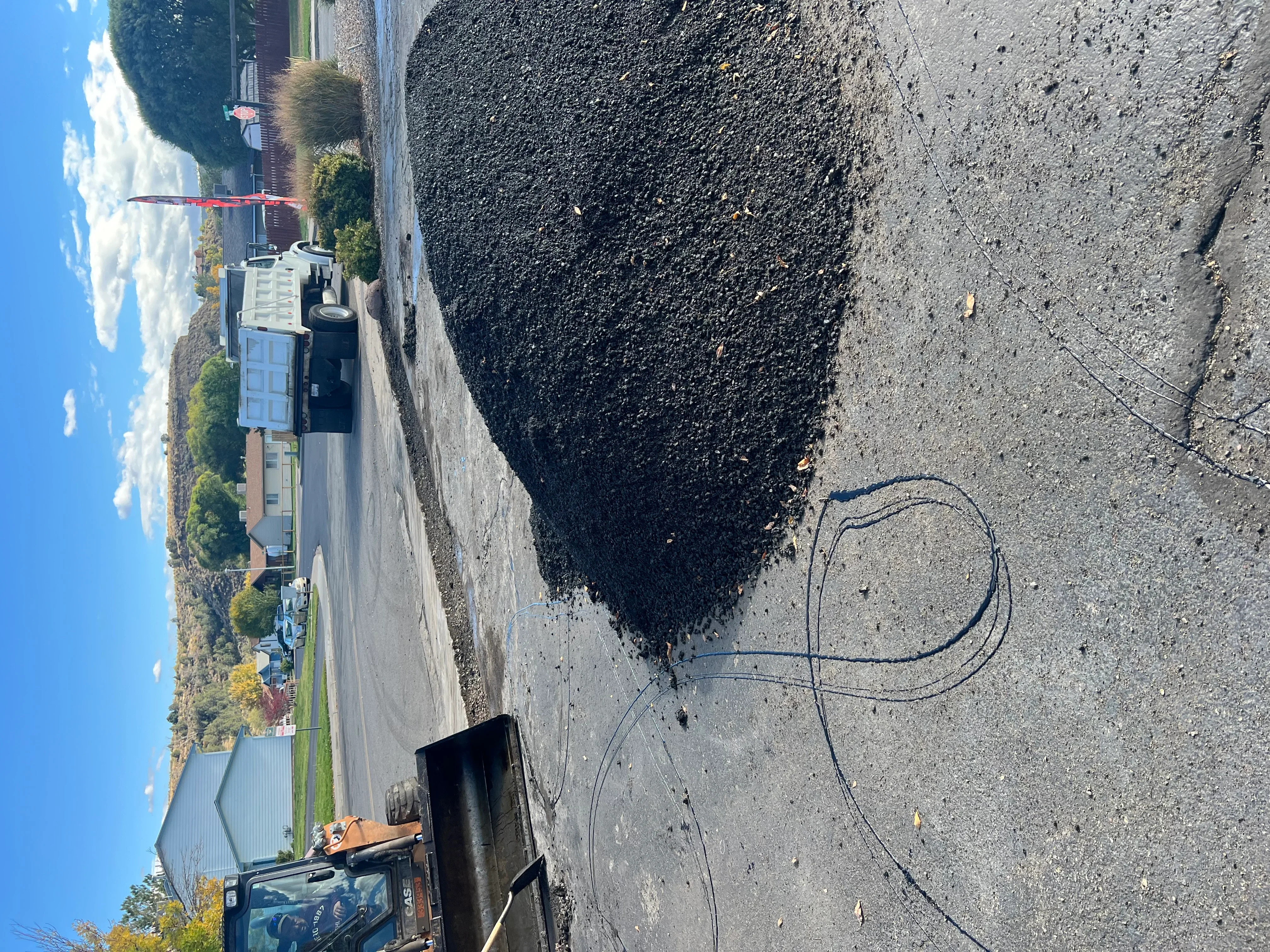 Fresh black asphalt driveway paving with compacted surface and equipment on residential property
