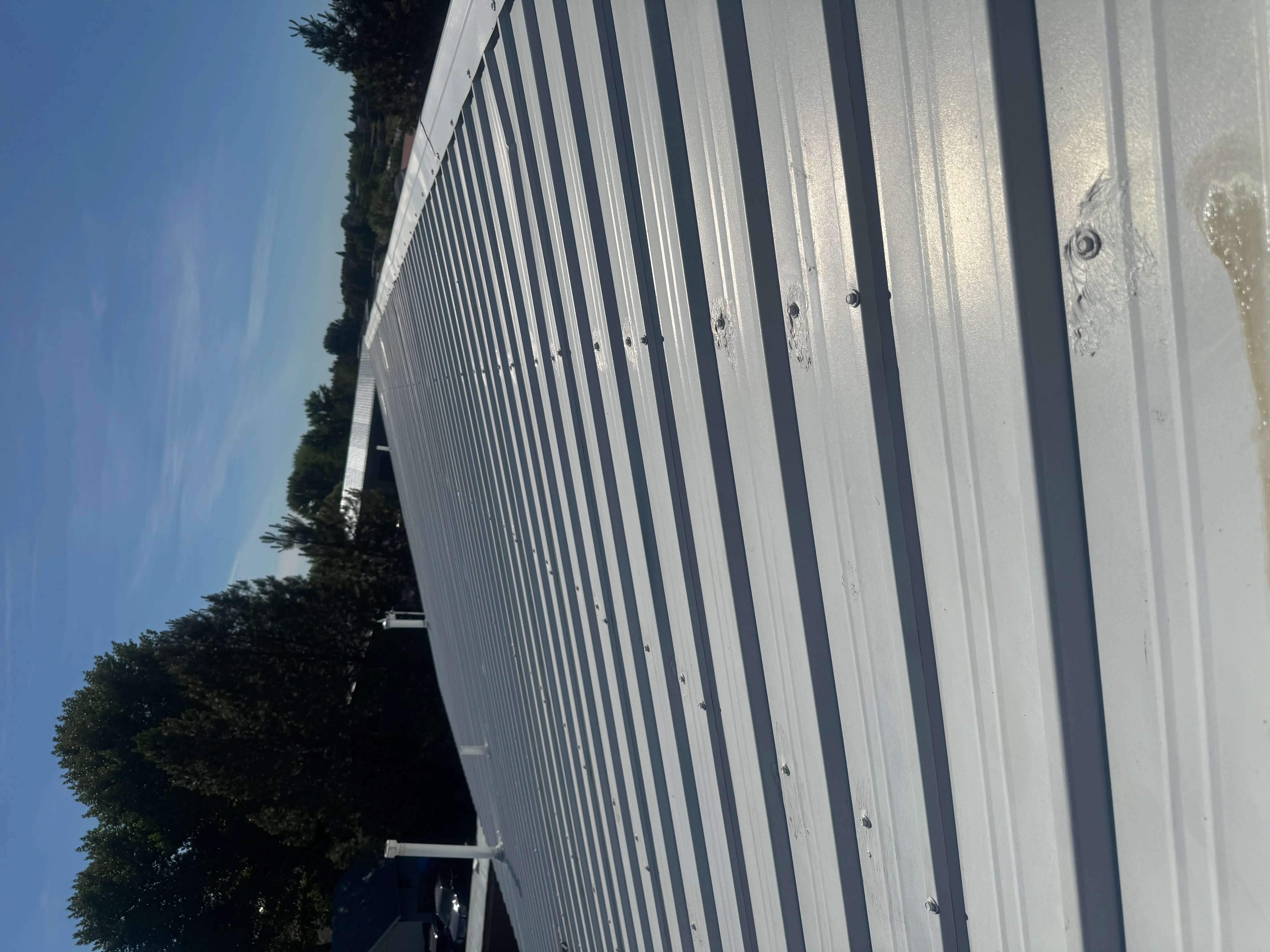 White corrugated metal roof panels with dark trim and fasteners installed on residential structure
